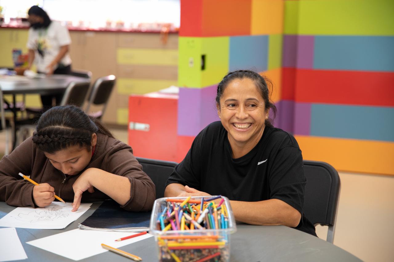 Woman smiling next to a girl writing